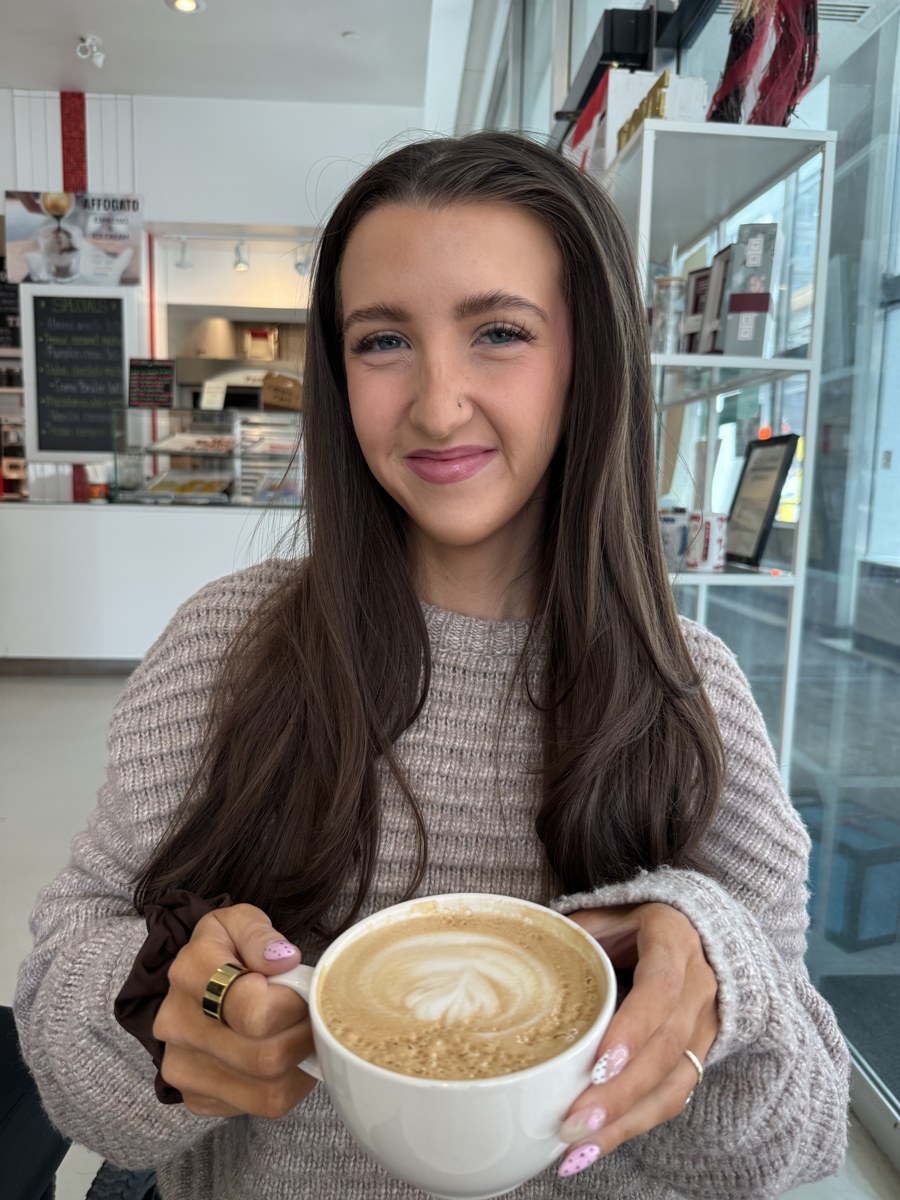 Kale Vine at a coffee shop in a red hoodie, holding a latte and looking at the camera