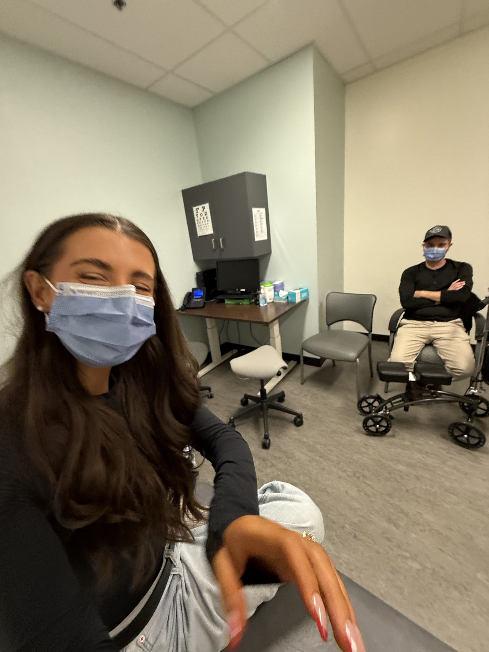 Kale Vine at a doctor's appointment with a knee scooter, Nick visible in the background