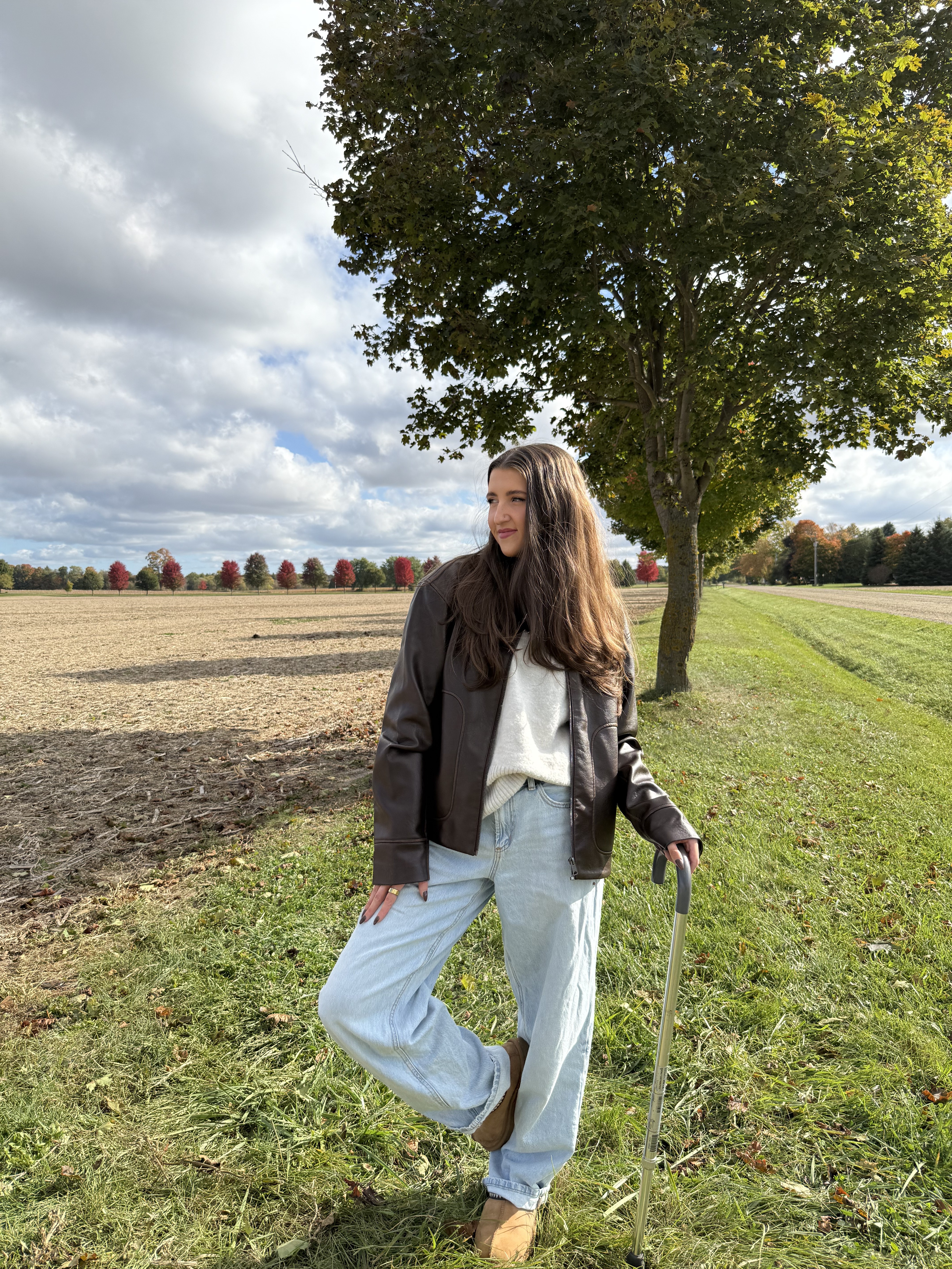 Kale Vine outdoors in autumn, dark leather jacket, holding a cane, dramatic open sky behind her