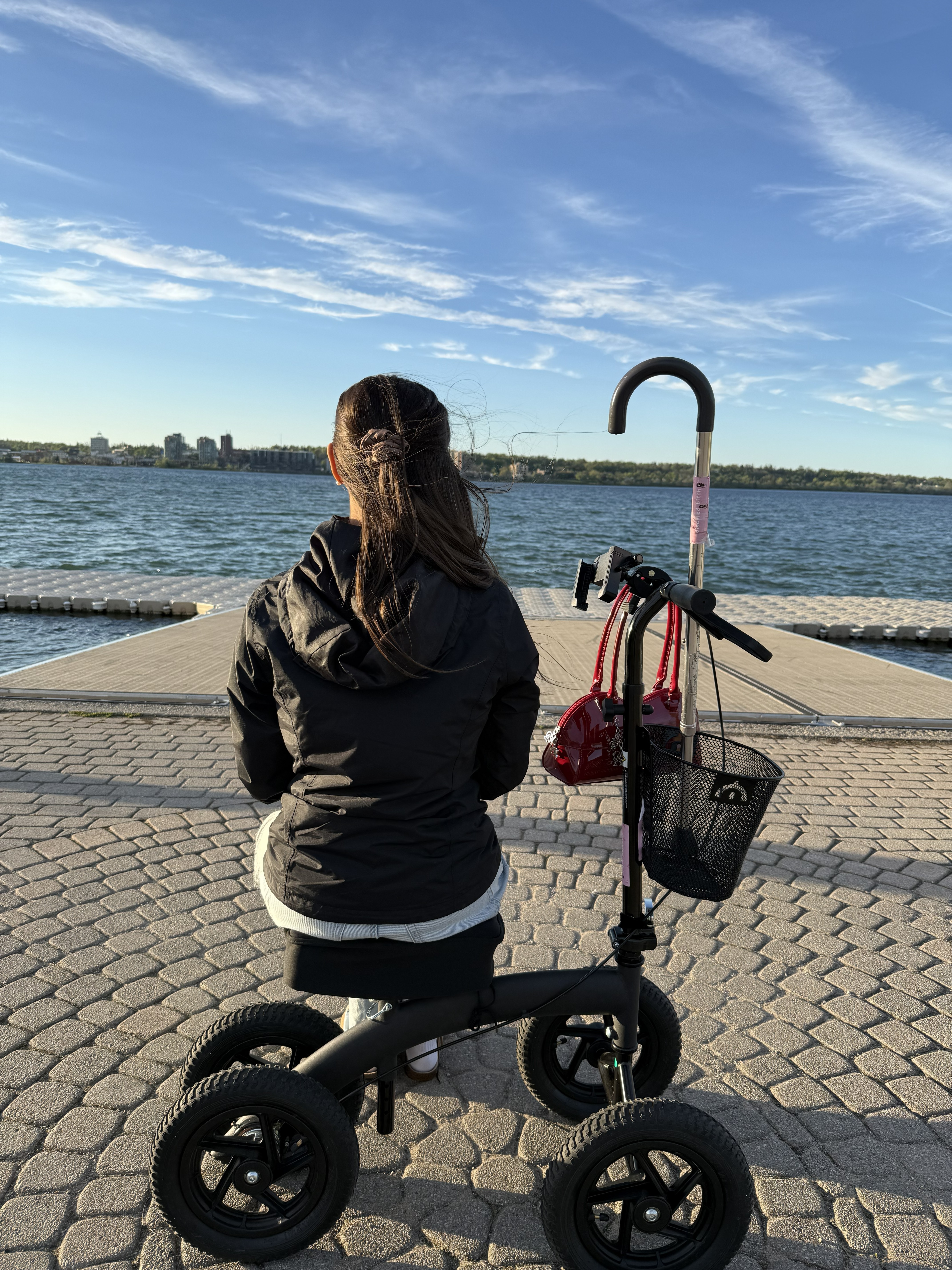 Kale Vine on a knee scooter silhouetted against a golden sunset, Toronto waterfront, city skyline reflected in the water