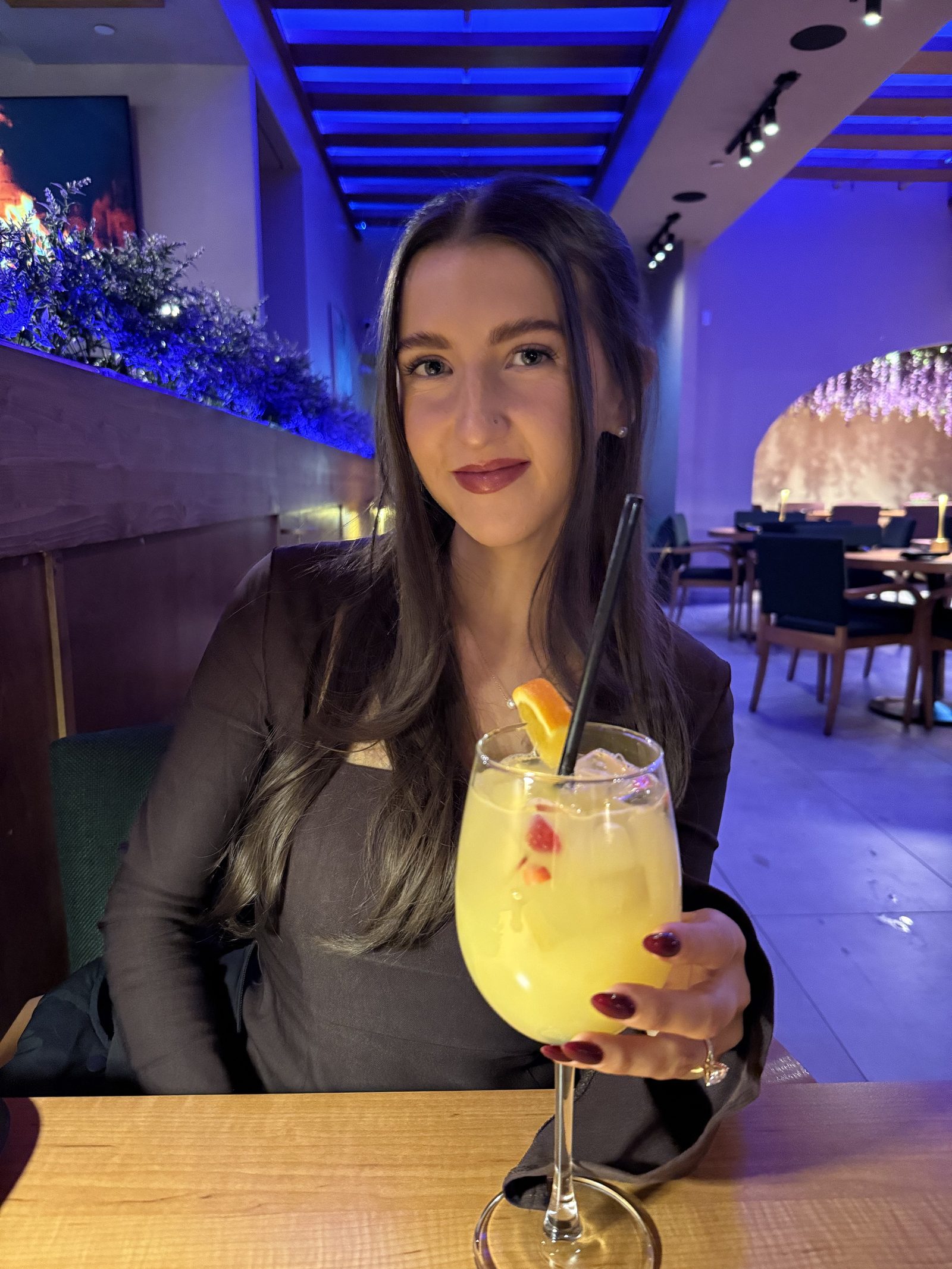 Kale Vine at a restaurant holding a cocktail, purple lighting