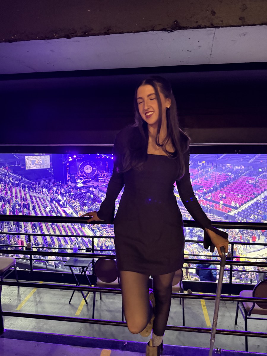 Kale Vine at a concert in a black mini dress, smiling, cane visible