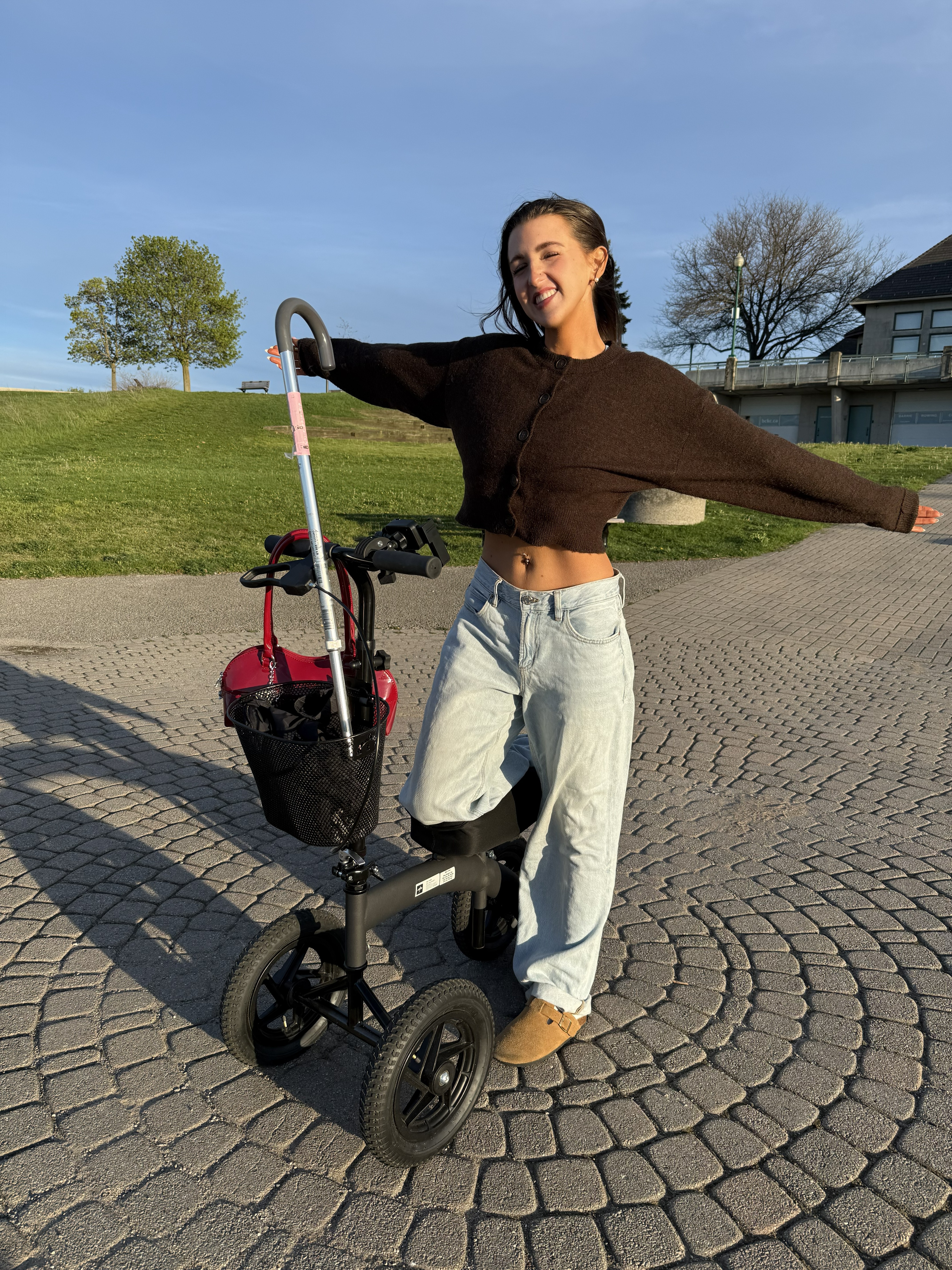Kale on her knee scooter, arms out, smiling